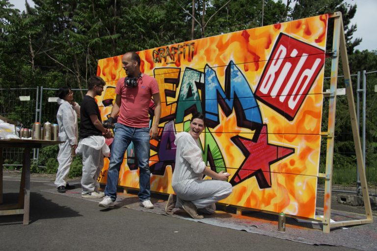 graffitiauftrag-graffitikuenstler-artmos4-bild-zeitung-workshop-graffiti-tag-style-schrift-logo-aussen-event-orange-bunt