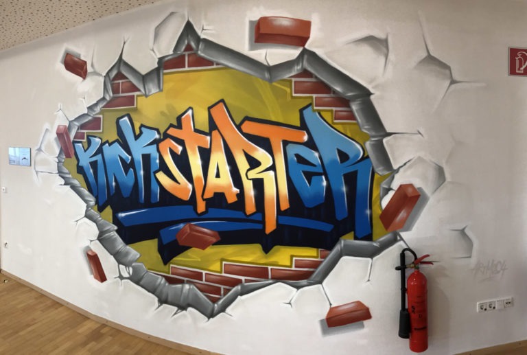 graffitiauftrag-graffitikuenstler-artmos4-bosch-kickstarter-schrift-graffiti-durchbruch-mauer-innen-blau-gelb-graffiti-technik