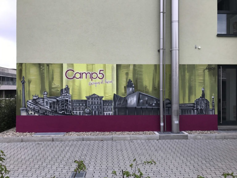 graffitiauftrag-graffitikuenstler-artmos4-camp5-schrift-skyline-landschaft-grau-pink-gruen-gelb-illustrativ-aussen