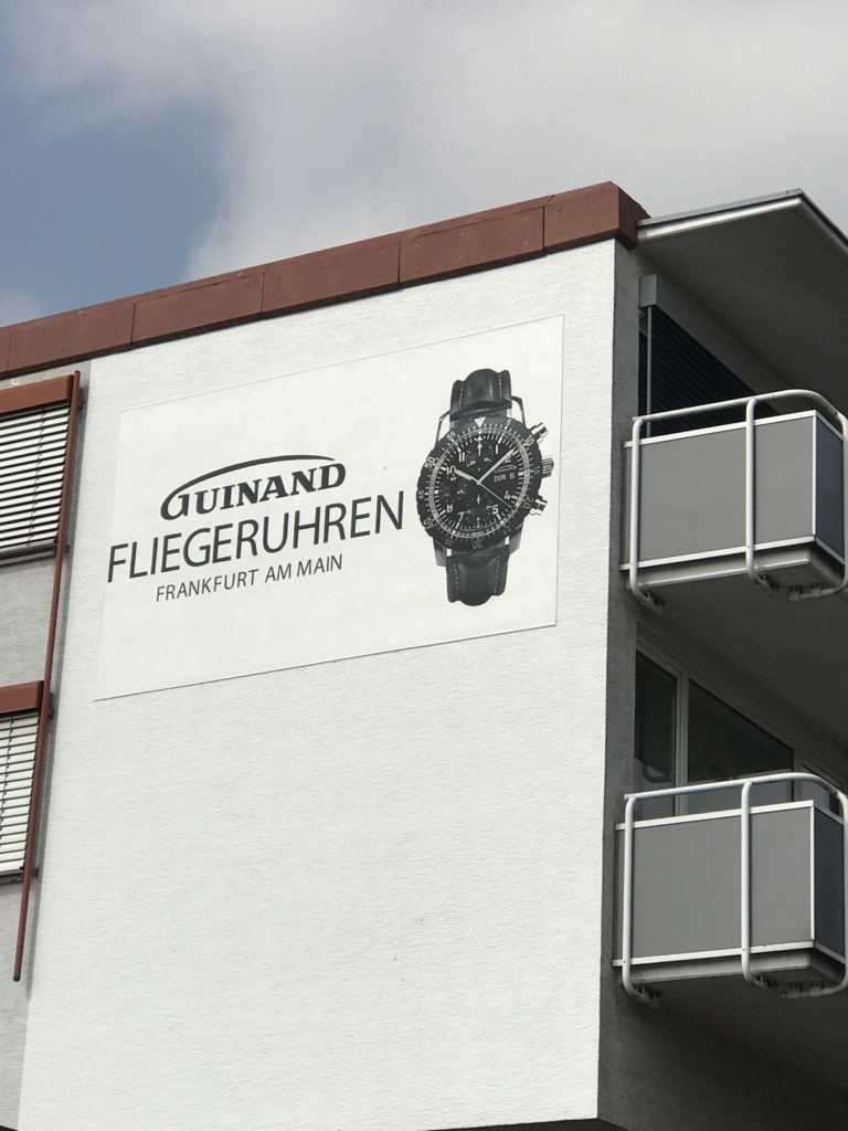 graffitiauftrag-graffitikuenstler-artmos4-guinand-fliegeruhren-frankfurt-schrift-uhr-schwarz-grau-fotorealistisch-aussen
