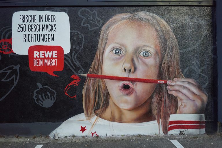 graffitiauftrag-graffitikuenstler-artmos4-rewe-skyline-obst-gesicht-schrift-wappen-aussen-schwarz-bunt-fotorealistisch-illustrativ-handel