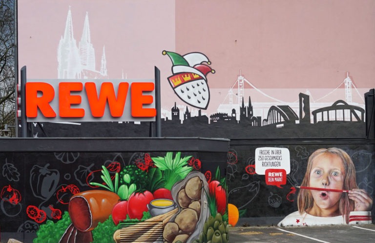graffitiauftrag-graffitikuenstler-artmos4-rewe-skyline-obst-gesicht-schrift-wappen-aussen-schwarz-bunt-fotorealistisch-illustrativ-handel